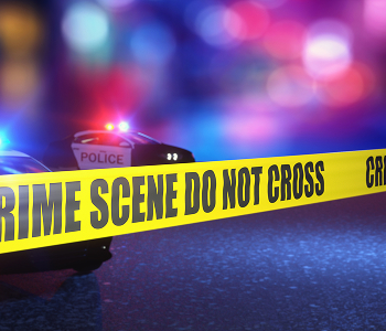 A police vehicle positioned beside yellow crime scene tape on the road