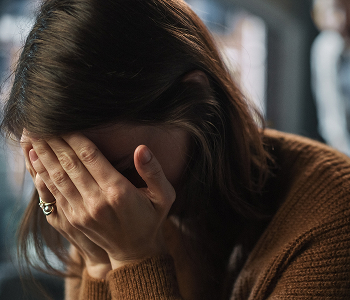 A woman with a distressed expression holds her face in her hands